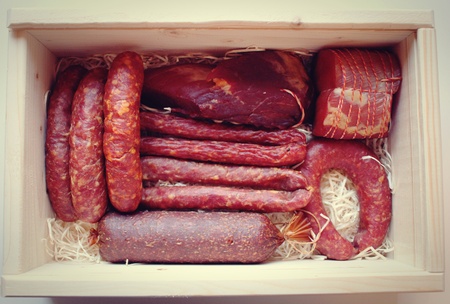 Assorted meat products including ham and sausages in a wooden box.の写真素材