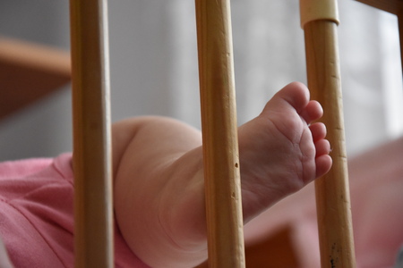 Baby, infant feet sticking out through the rails of a crib, cot, beautiful background for card,  banner, wallpaper designの写真素材