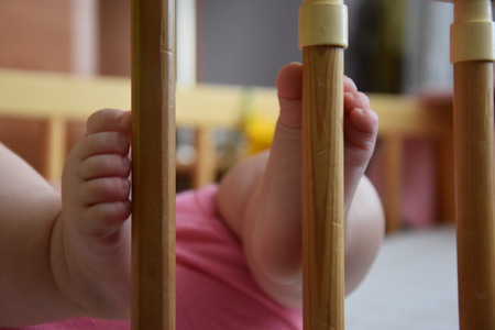 Baby, infant feet sticking out through the rails of a crib, cot, beautiful background for card,  banner, wallpaper designの写真素材