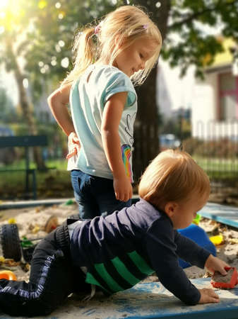 Sister and brother playing with sand. Adorable little kids family related in sandbox on playground. Happiness of play together outside. sibling leisure activity. older girl child looking after boy.の写真素材