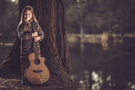 Girl With Guitar in the Park. Little Caucasian Girl with Acoustic Guitar in Hands. Young Guitarist.の写真素材