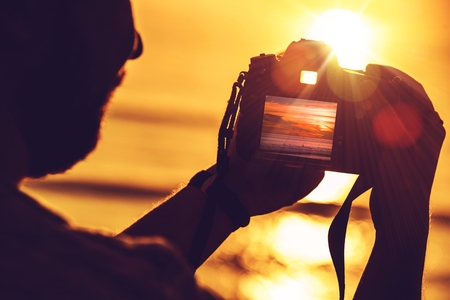 Travel Digital Photography Concept Photo with Men Playing His Professional Digital SLR Camera During Sunset.の写真素材