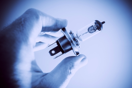 Car Headlight Bulb in Hand. Blue Color Grading. Modern Transportation Safety Lighting.の写真素材