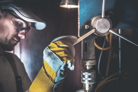 Small Drill Works in a Garage. Caucasian Men Using Metal Driller Machine.