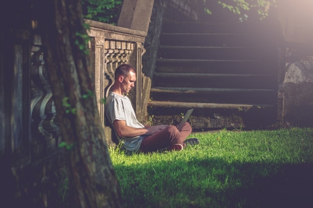 Learning Student with Laptop in the Very Old City Park. Summer Time Learning.の写真素材