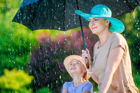 Caucasian Mother with Daughter Under Large Umbrella During Summer Rain.の写真素材