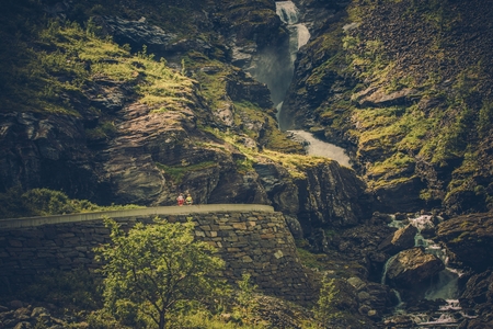 Scenic Norwegian Mountain Trail Road. Two People on the Winding Mountain Road with Large Waterfalls.の写真素材