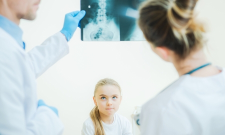 Little Girl Awaiting Medical Diagnosis in Front of Two Hospital Physicians with X Ray Image.の写真素材