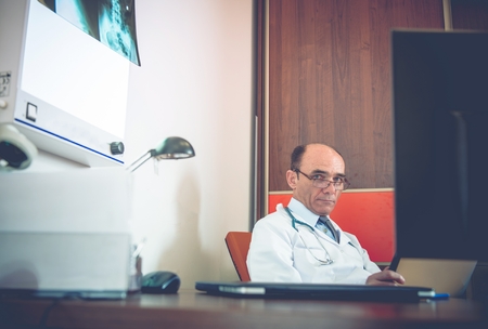 Medical Doctor in His Office. Doctor Researching Test Results on His Mobile Tablet Device.