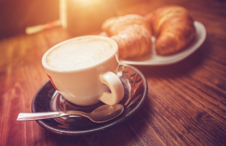 Cappuccino Coffee Time. Freshly Made Cappuccino and Tasteful Croissants on the Wooden Table Somewhere in the Italy.の写真素材