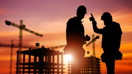Commercial Construction Concept with Silhouette of Two Workers Wearing Hard Hats and Construction...