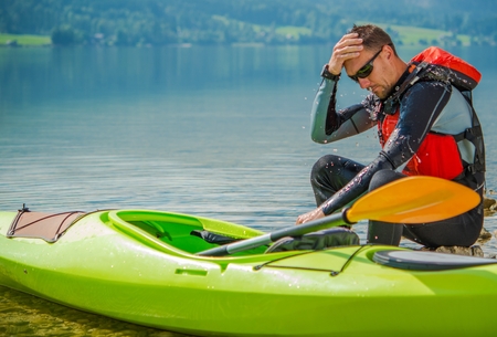 Resting Kayaker on the Rocky Lake Shore. Young Caucasian Kayaker with His Kayak.の写真素材