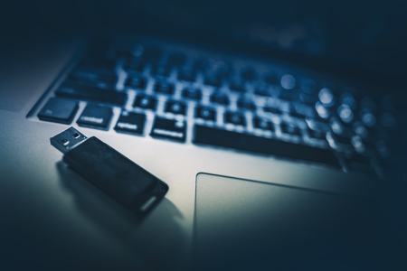 Pen Drive Memory Stick on the Laptop Computer. Dark Blue Color Grading.