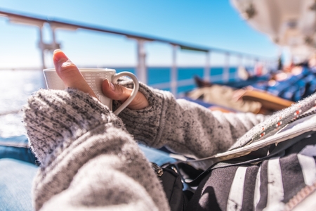 Cup of Coffee on the Cruise Ship Deckchair During Ocean Crossing. Woman Wearing Sweater Holding...
