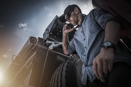 Transportation Industry Business. Caucasian Semi Truck Driver in His 30s Talking with Client Over the Phone While Seating on His Truck. Business Phone Call.の写真素材