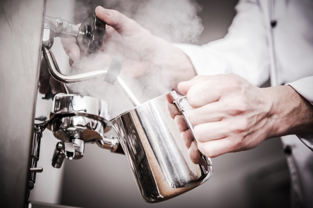 Italian Barista Milk Steaming in the Stainless Steel Milk Pitcher. Closeup Photo. Preparing Fresh Espresso Based Cappuccino.の写真素材