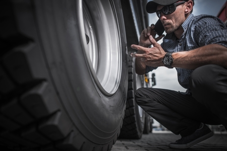 Truck Driver Ordering New Wheels For His Semi Truck. Caucasian Worker Phone Conversation While Looking on the Rear Side of His Trailer Axle.の写真素材