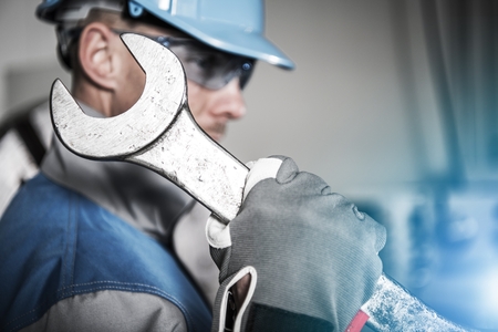 Worker with Huge Iron Wrench Spanner. Heavy Duty Maintenance Concept. Caucasian Technician in Blue Hard Hat.の写真素材