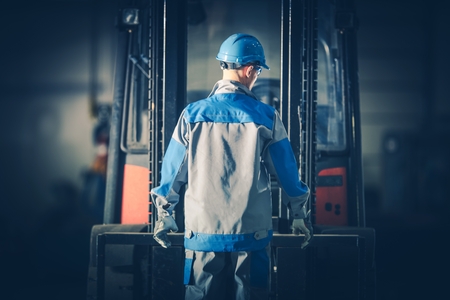 Caucasian Warehouse Forklift Operator in Front of His Lift Truck. Moving and Lifting Equipment.