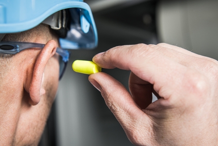 Ear Plugs Hearing Protection Simple Solutions. Factory Worker in Blue Hard Hat Preparing To Use...