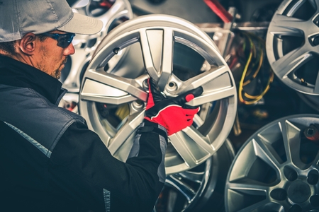 Buying New Alloy Wheels and Seasonal Tires Change Concept Photo. Caucasian Car Service Worker with Large Rim in Hands.の写真素材