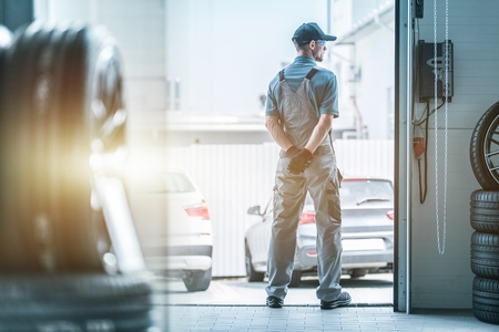 Caucasian Auto Service Worker Waiting For Clients Standing in the Garage Gate. Automotive Business Concept.の写真素材