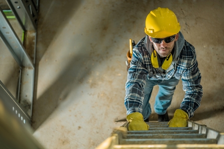 Smiling Caucasian Construction Contractor on a Ladder Going Up Toward Second Floor.の写真素材