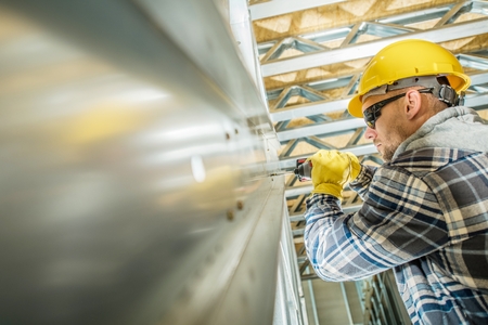 Building Steel Frame Contractor Worker Closeup Photo. Caucasian Men with Drill Driver Connecting Steel Elements of the Frame.の写真素材
