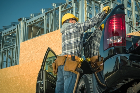Construction Industry Business. Caucasian Contractor Worker in Front of the Newly Built Structure Looking For Tools Inside His Pickup Truck.の写真素材