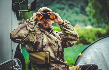 Hunting Season Game Spotting. Caucasian Hunter with Binoculars and the Campsite in Background.の写真素材