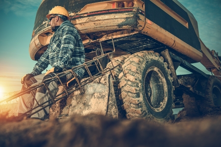 Caucasian Construction Site Excavating Worker Wearing Yellow Hard Hat. Excavator and a Reinforcement Steel Elements.の写真素材