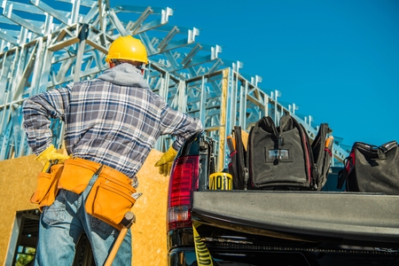 Construction Contractor Job. Caucasian Worker Wearing Yellow Safety Hard Hat in Front of Newly Developed Building.の写真素材
