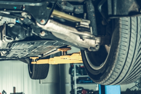 Modern Car in Auto Service. Vehicle on a Lift Awaiting Repair by Professional Mechanic. Automotive...