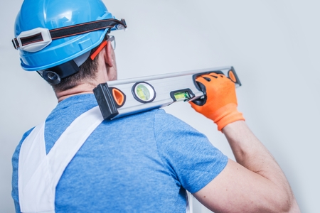 Caucasian Construction Worker with Spirit Level Tool on His Shoulder. Men Wearing Blue Hard Hat.