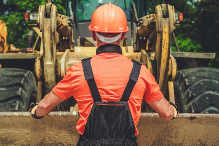 Worker and the Bulldozer. Caucasian Heavy Duty Equipment Operator in His 30s in Front of the Machine.の写真素材