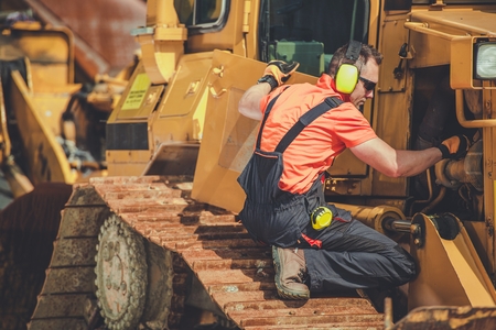 Bulldozer Professional Mechanic. Caucasian Technician Taking Machine Under Maintenance. Construction Heavy Duty Equipment.の写真素材