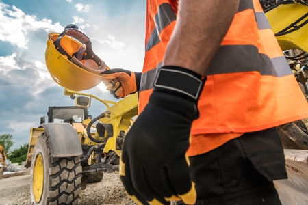 Hard Hat Construction Safety. Caucasian Heavy Duty Equipment Operator is About to Wear His Yellow...