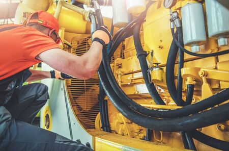 Caucasian Professional Mechanic Fixing Bulldozer Engine Inside Heavy Equipment Repair Shop.の写真素材