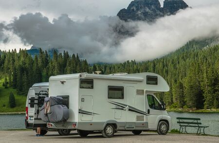 Scenic Camper Camping. Two Motorhomes on the Lake Shore. Scenic Cloudy Mountain Range in a Background. Recreational Vehicle Road Trip.の写真素材