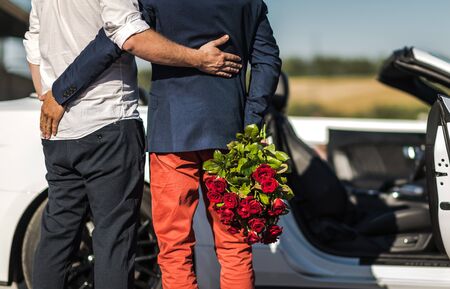 Same SexRelationship. Gay Couple in Front of a Car. One Men with Bouquet of Red Roses.の写真素材