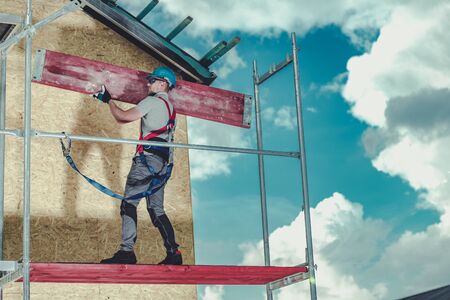 Construction Scaffolding Installation by Caucasian Contractor Worker. Safety Harness and Hard Hat...