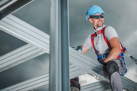Smiling Construction Contractor Wearing Safety Harness. Caucasian Worker in His 30s. Skeleton Steel Building Frame.の写真素材