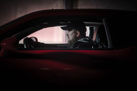 Muscle Car Night Drive. Young Caucasian Men in His 20s Wearing Black Baseball Hat Driving His Car Late Night Hours. Transportation Theme.の写真素材