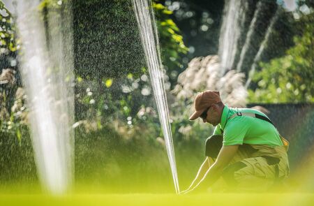 Garden Watering System Installation. Caucasian Worker Adjusting Water Sprinkler. Gardening...