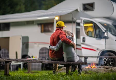 RV Campsite Family Time. Father Hugging His Daughter on Wooden Bench in Front of Campfire and...
