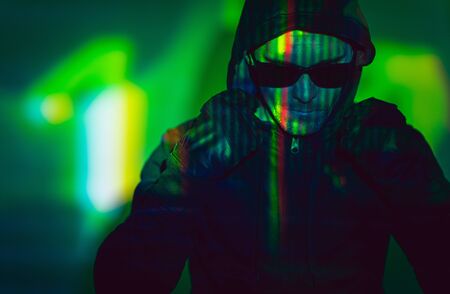 Caucasian Hacker Wearing Hood and Sunglasses Hiding His Face. Greenish Illumination Concept Photo.の写真素材