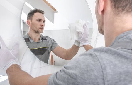 Caucasian Men Cleaning Circular Bathroom Mirror Using Paper Towel. Finishing Newly Remodeled Bathroom.の写真素材