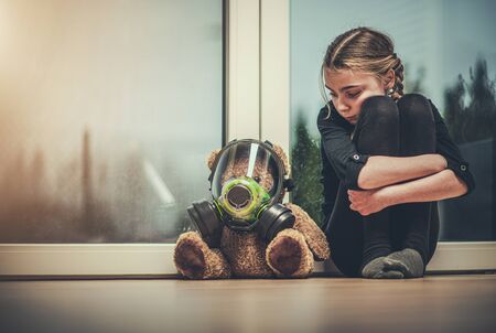 Virus Outbreak Theme. Caucasian Girl Protected Her Teddy Bear with Safety Breathing Biochemical Mask. Seating Together on a Floor Awaiting End of Pandemic.の写真素材