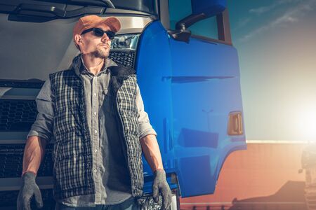 Transportation Industry Theme. Caucasian Truck Driver in His 30s in Front of His Modern Blue Semi...
