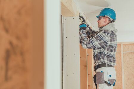 Male Electrician Contractor Feeding Electric Wire Through Wooden Framing In New House Construction. 